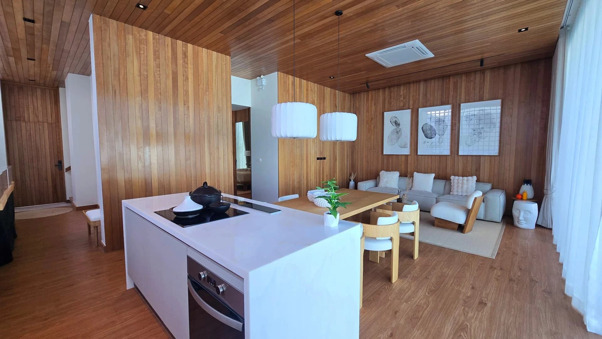 Kitchen island with induction hob and built-in oven, dining and lounge behind, timber walls and ceiling
